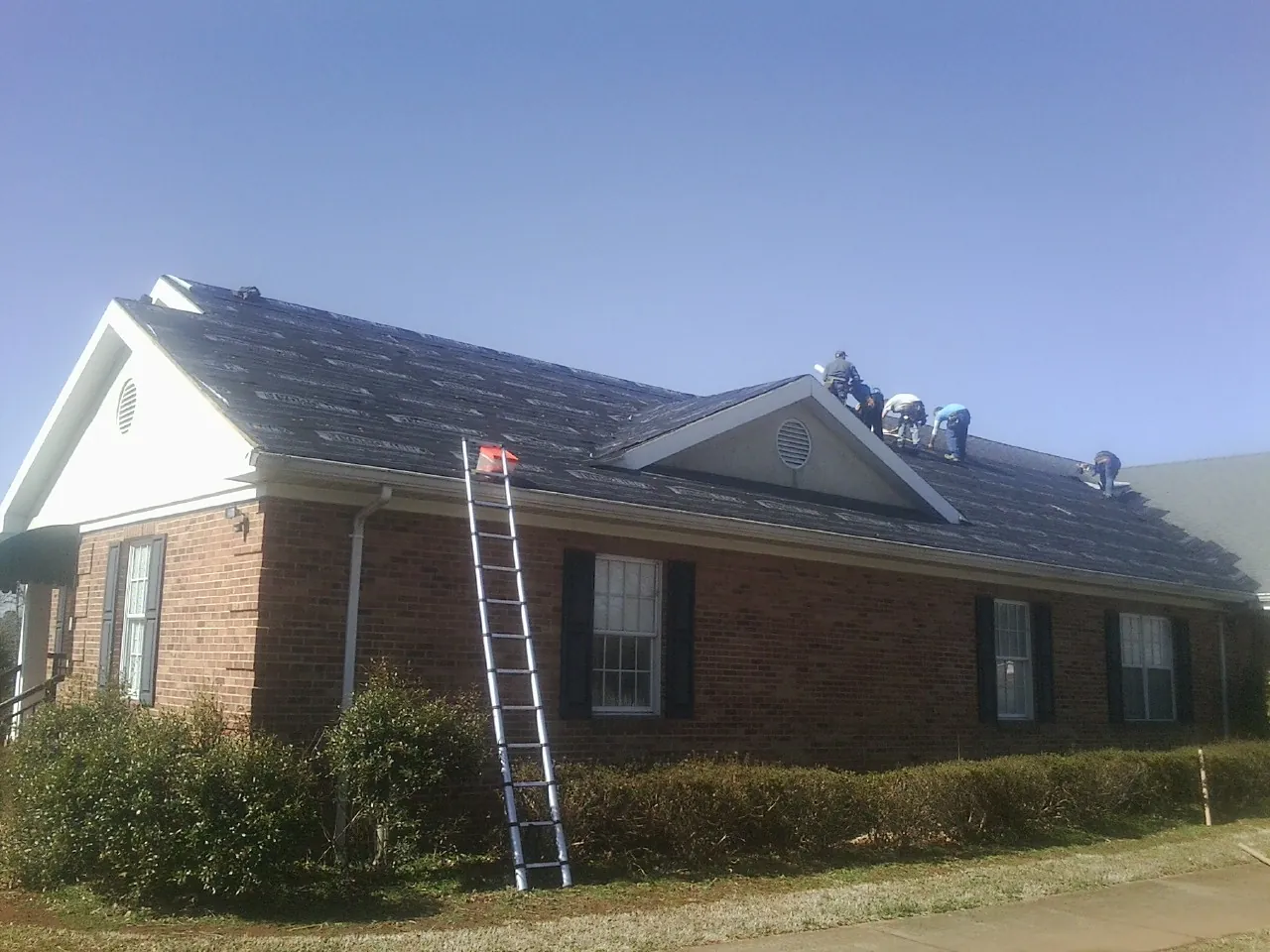 Crew tearing shingles off a brick ranch roof with a ladder set — Emergency Roof Repair work by our crew in Crabtree