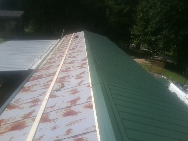 Old rusted panels beside newly installed green metal roofing — Wind Damage Roof Repair by Roofing Brothers in Crabtree