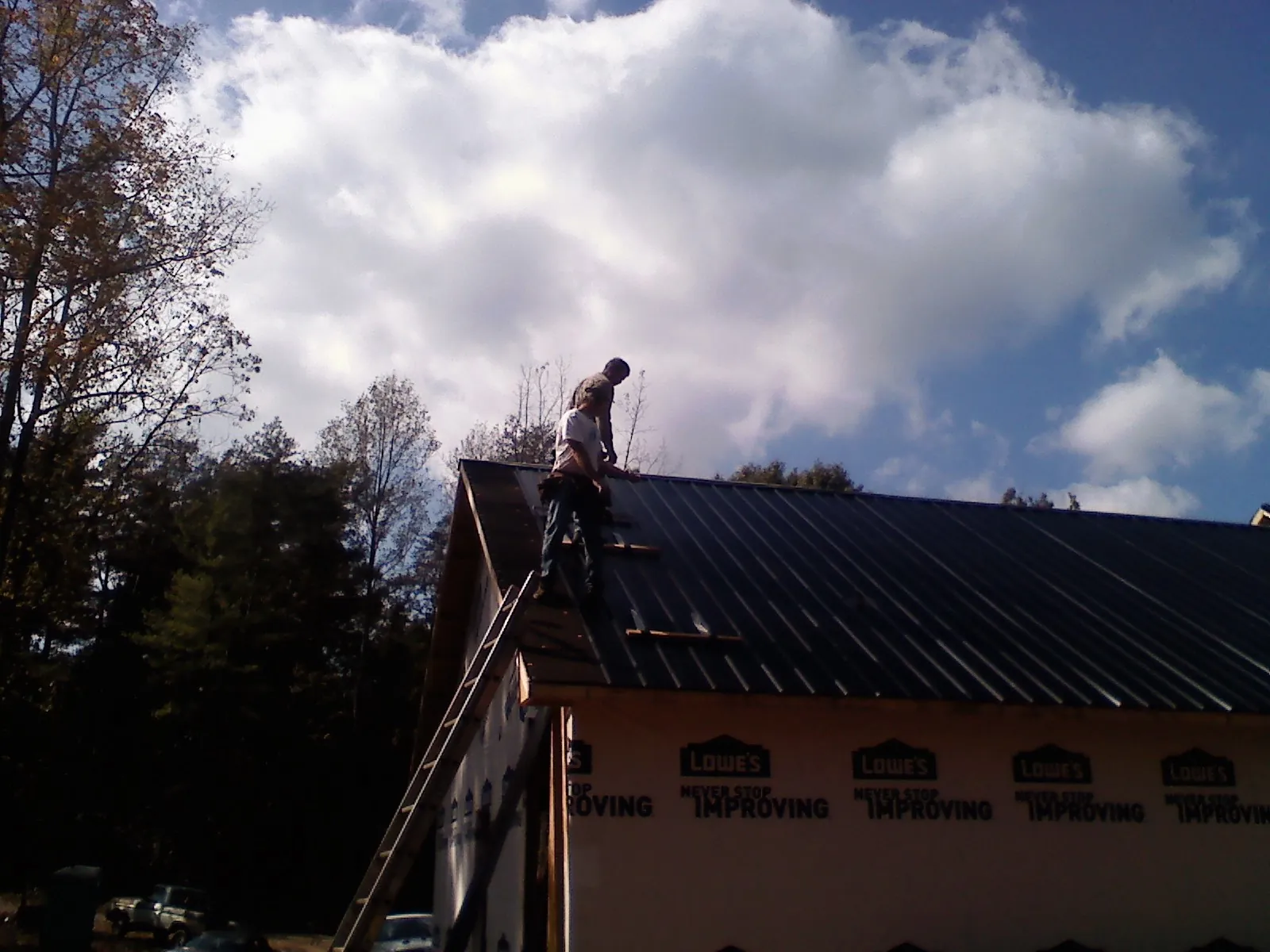 Roofer fastening dark metal panels high against a cloudy sky, from a Roof Inspection job in Crabtree