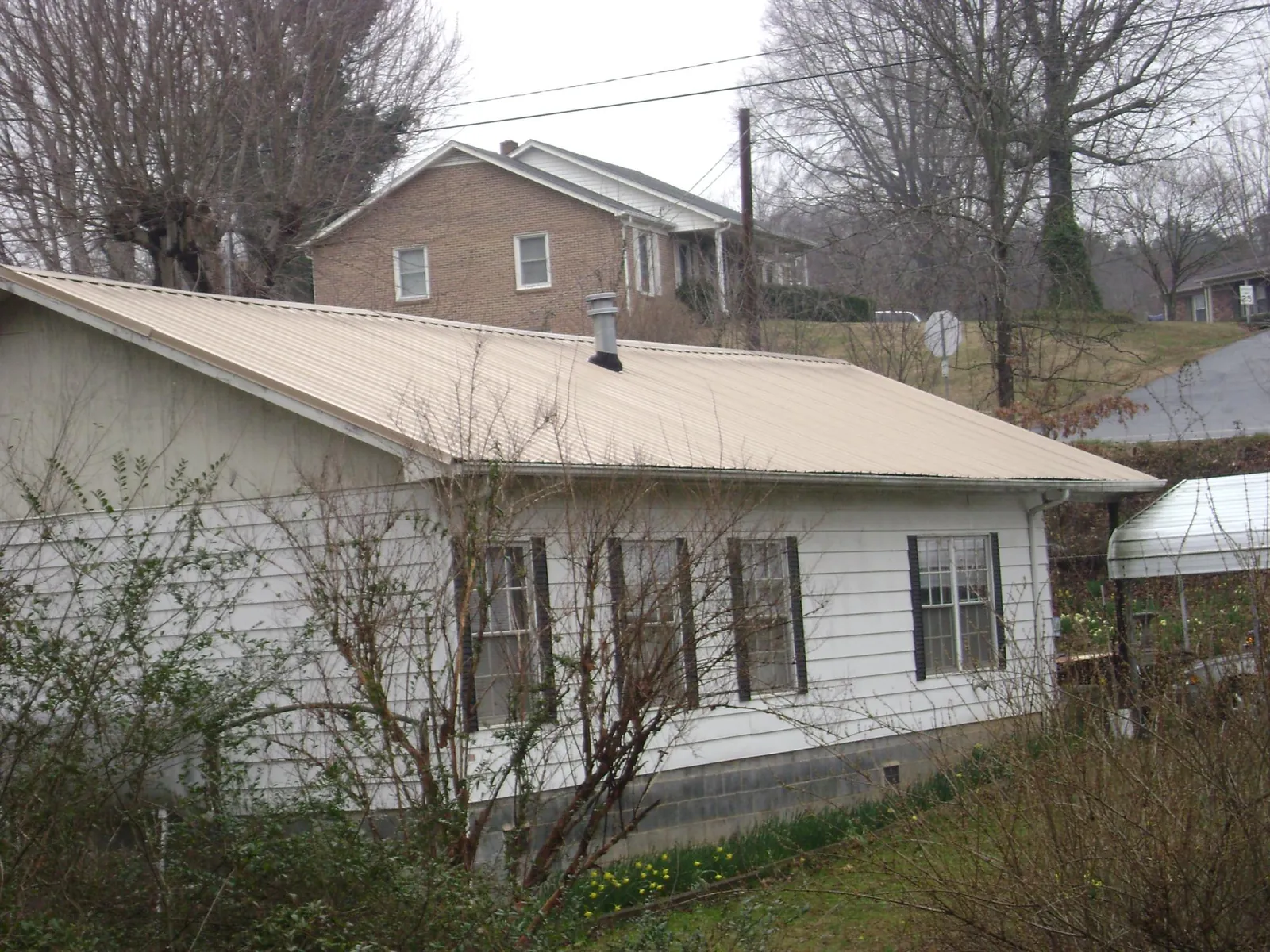 Tan metal roof on a white sided house set into a hillside in Crabtree