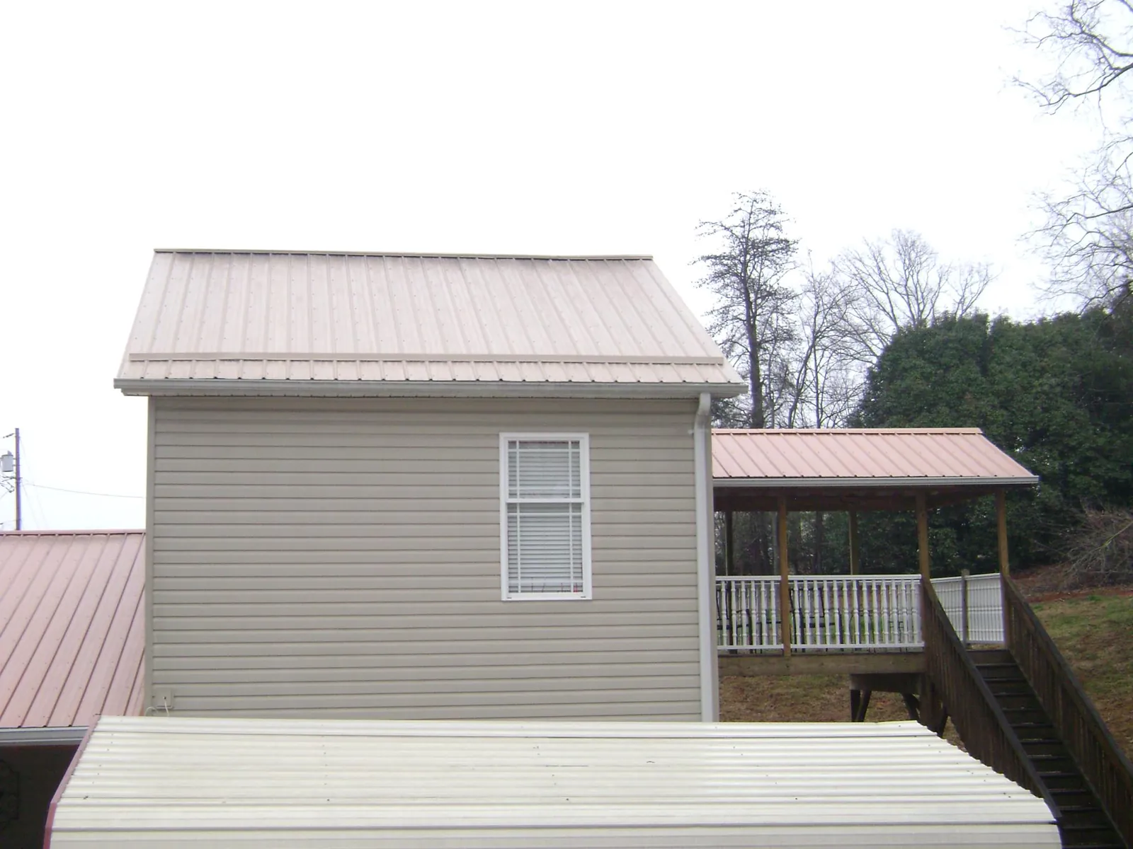 Tan metal roofs on a two story addition and attached porch, from a Roof Replacement job in Crabtree